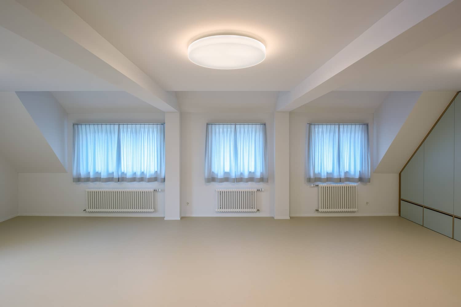 An der Fensterfront in einem leeren Raum h&auml;ngen massgeschneiderte Tagesvorh&auml;nge